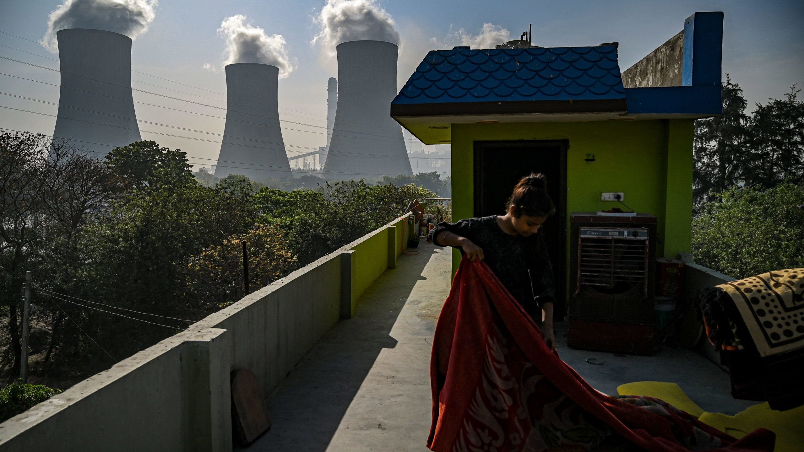 A girl folds a blanket at her house rooftop near the Thermal Power Corporation (NTPC) plant in Dadri, India. Photo by PRAKASH SINGH/AFP via Getty Images
